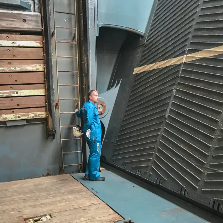 A man in a blue jumpsuit inspecting hydraulic stern ramp