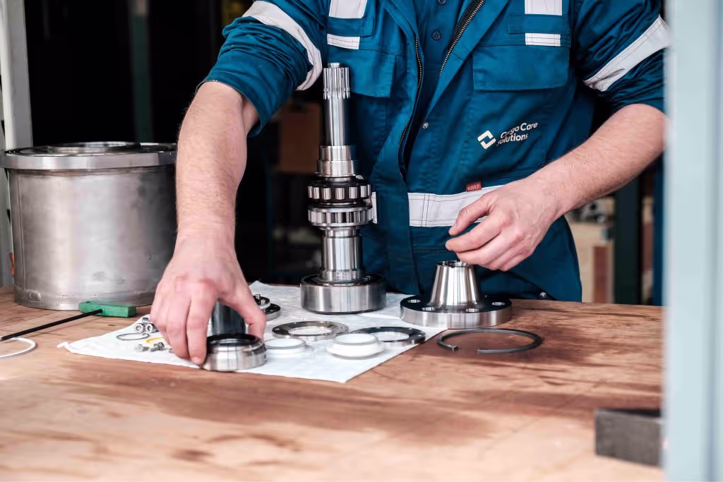 A man wearing a blue shirt and white pants is working on a cargo pump.