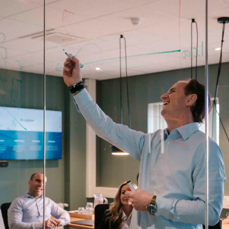 A man in a blue shirt writing on a glass wall.