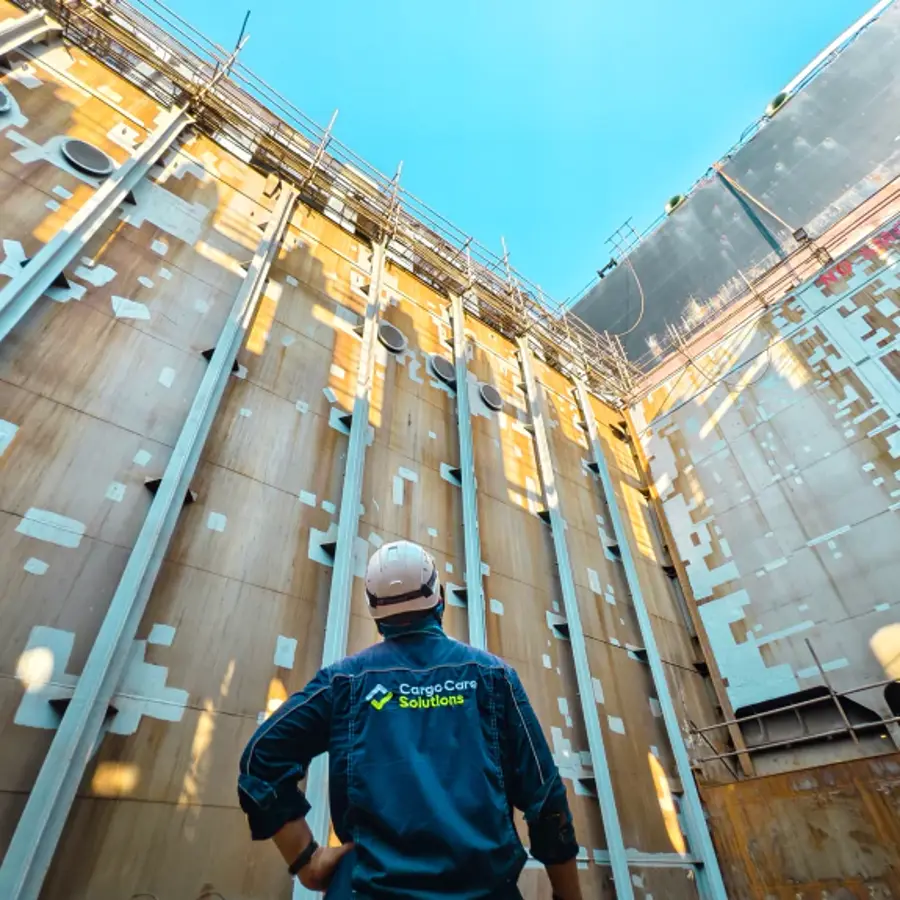 A man in a blue jumpsuit standing in a container ship looking up