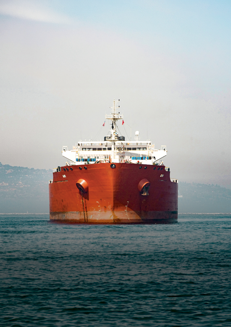 Red-hulled tanker at anchor, seen head-on from the water